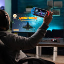 Jugador con auriculares en escritorio sosteniendo consola portátil X7 Ecuador frente a monitor con mensaje You Win
